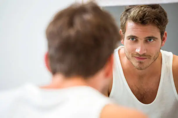 Smart young man looking at himself in mirror at bathroom