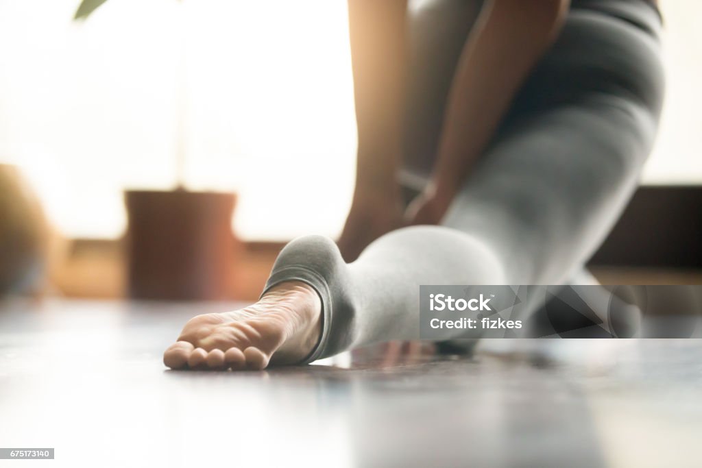 Young yogi woman in anjaneyasana pose, home background, close up Young woman practicing yoga, stretching in anjaneyasana exercise, Horse rider pose, working out, wearing sportswear, grey pants, indoor, home interior, living room close up, foot in the focus Pilates Stock Photo