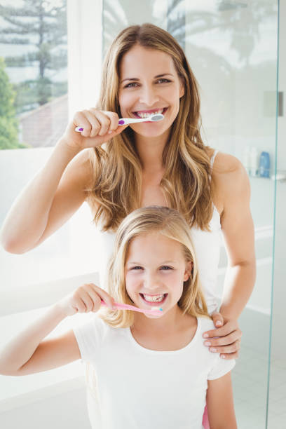portrait of smiling mother and daughter brushing teeth - human teeth child smiling family imagens e fotografias de stock