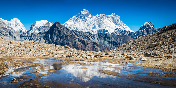 The iconic summit pyramid of Mt. Everest (8848m), Nuptse (7861m) and Lhotse (8516m) towering over the snow capped peaks and dramatic mountain pinnacles of the Himalayas reflecting in an icy lake high in the winter wilderness of the Sagarmatha National Park, Nepal.