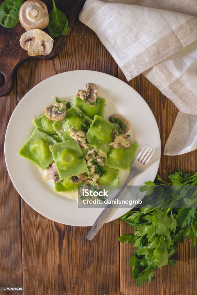 Delicious green dumplings with spinach dough stuffed with cheese with champignon sauce. Italian Cuisine. Delicious green dumplings with spinach dough stuffed with cheese with champignon sauce. Italian Cuisine. On a wooden background Ravioli Stock Photo