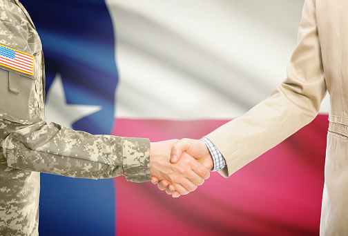 American soldier in uniform and civil man in suit shaking hands with USA state flag on background - Texas