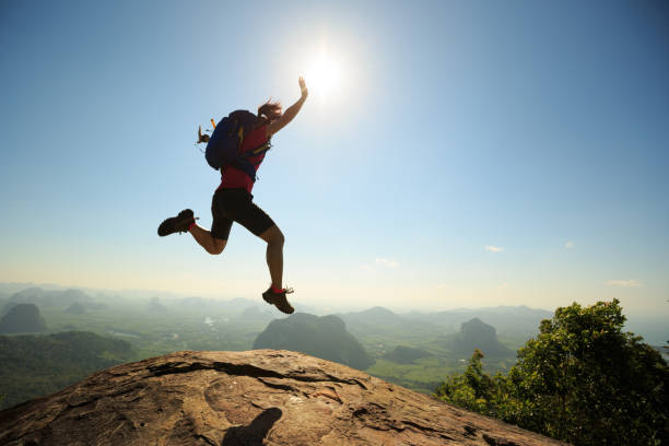 istock cheering successful young woman hiker jumping on mountain peak 675286140