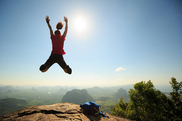 istock cheering successful young woman hiker jumping on mountain peak 675286402