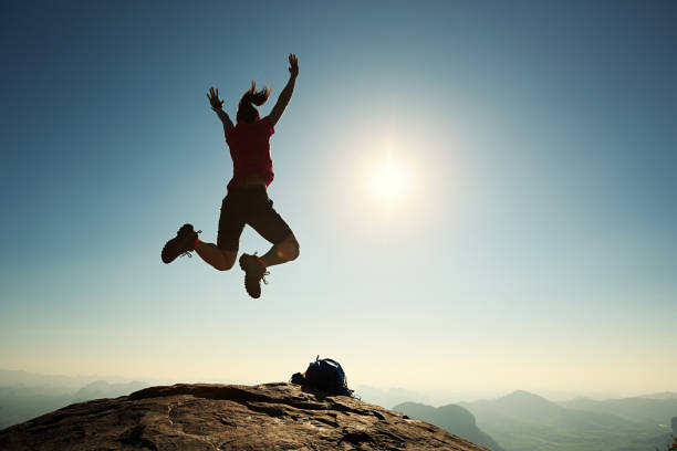 istock cheering successful young woman hiker jumping on mountain peak 675288938
