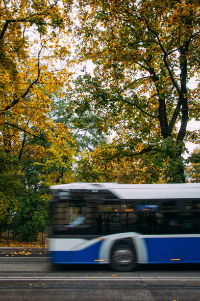 A blue public bus moves across the frame down the street with trees and foliage in the background in autumn. Abstract, motion blur. stock photo