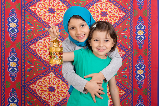 Happy Family in Ramadan - Two Muslim sisters celebrating Ramadan - playing with Ramadan lantern in front of Ramadan background