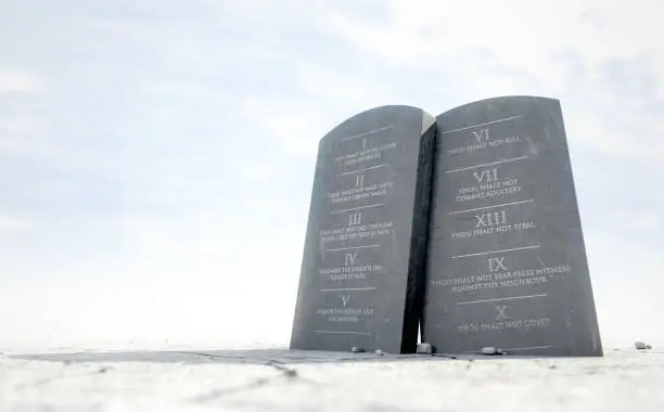 Two stone tablets with the ten commandments inscribed on them standing in brown desert sand infront of a blue sky - 3D render