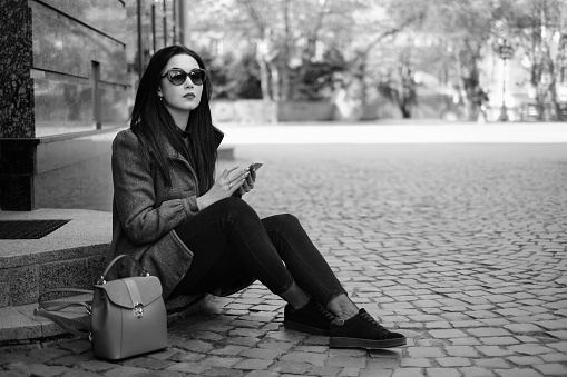 Young brunette girl sitting on the street with cellphone, black and white