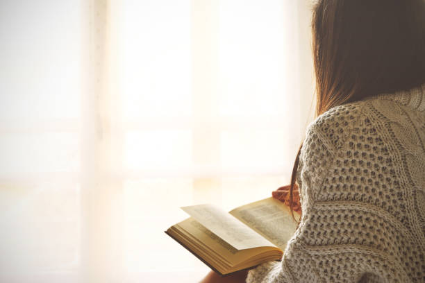 istock Young woman sitting in bed while reading a book 675337092