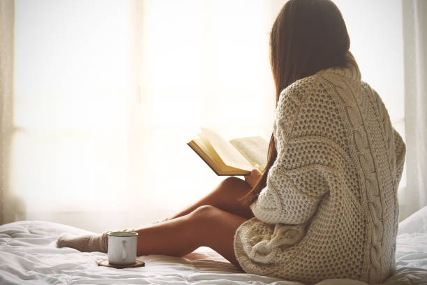 Jeune femme assise dans son lit en lisant un livre - Photo