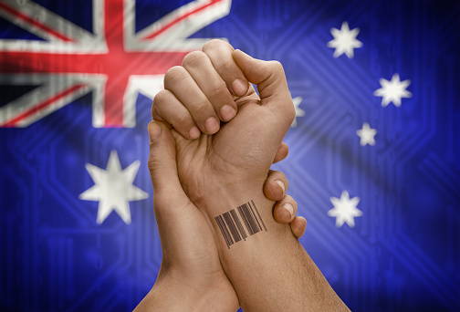 Barcode ID number tattoo on wrist of dark skinned person and national flag on background - Australia