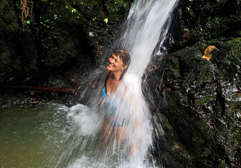 A woman stands under the streams of a waterfall