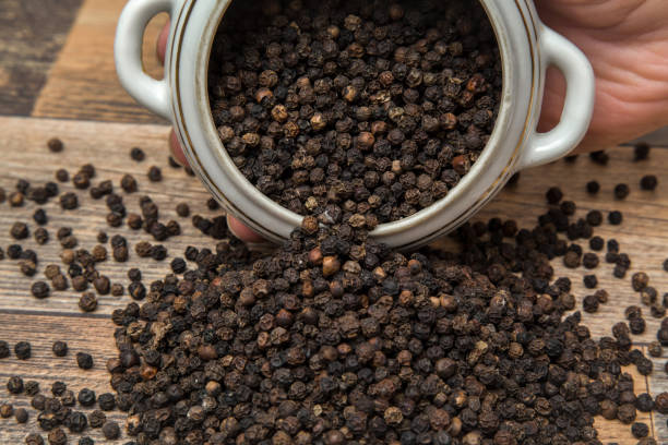 Black pepper grain in the bowl on the table in the kitchen. Healthy eating and lifestyle. stock photo