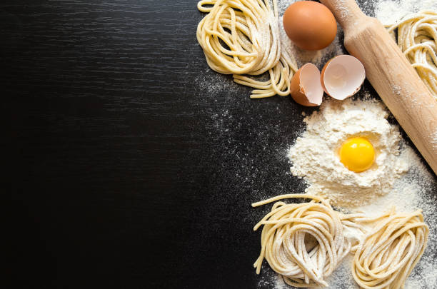 Raw homemade pasta with ingredients on black background.