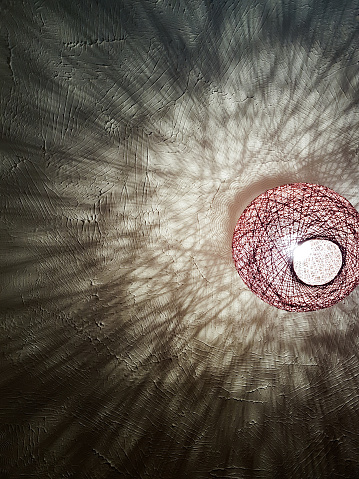 A lightshade throws abstract shadow patterns onto a white ceiling
