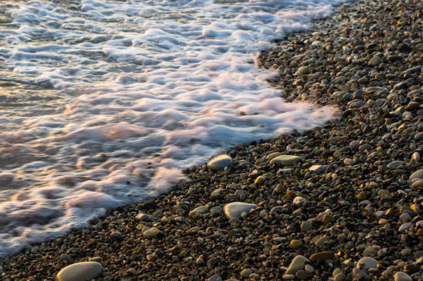 istock sea pebble beach with multicoloured stones, waves with foam 675422972