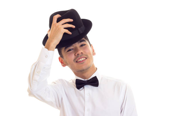 Happy young man in white shirt with black bow-tie and black hat on white background in studio