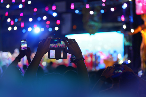 Audience spectators taking smart phone photos at a colorful entertainment performance.