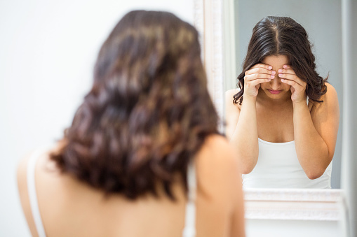 Unhappy woman standing in front of mirror in bathroom