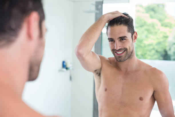 istock Shirtless young man smiling while looking in mirror 675457884
