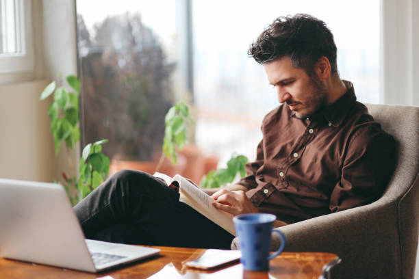istock Young man reading a book at home 675469256