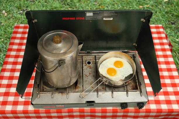 A well used camping stove is being used to fry eggs and make coffee.