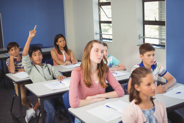istock School kids raising hand in classroom 675473010