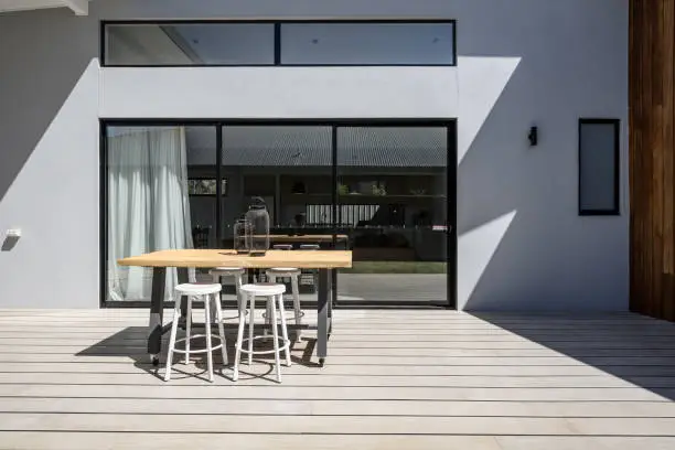 Sunny outdoor entertaining deck with triple glass sliding doors at a new contemporary designed home
