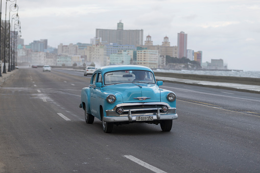 Vintage cars are driving on the street. Incidental people on the background.