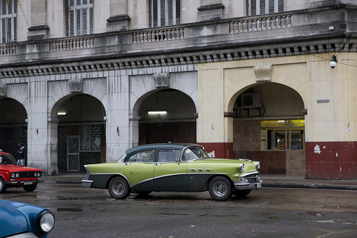 Vintage cars are driving on the street. Incidental people on the background.