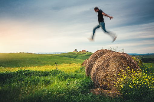 Man jumping from hay bales in Tuscany (Val D'orcia, Italy).