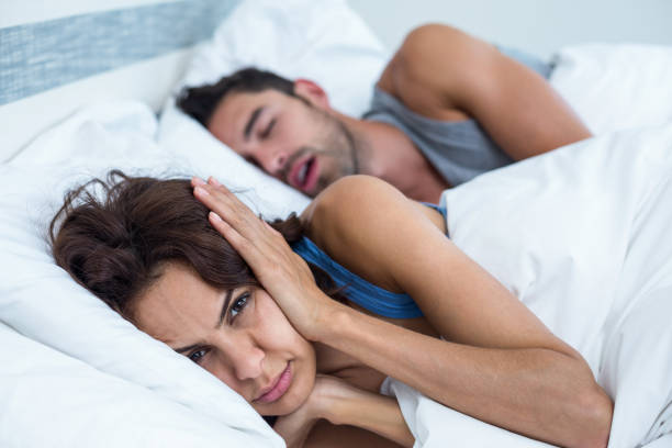Woman blocking ears with hands while man snoring on bed stock photo