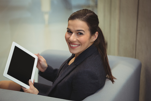 Happy businesswoman sitting on sofa and using digital tablet in office