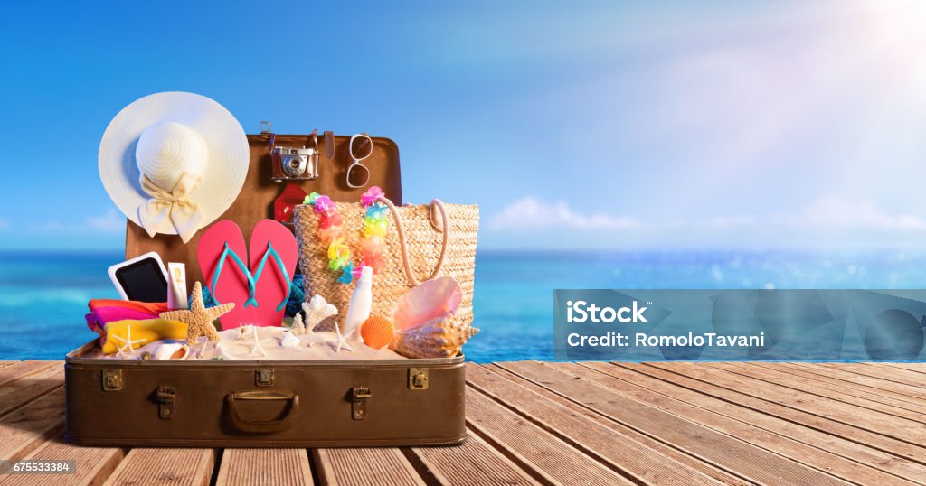 Beach Accessories In Suitcase On Beach - Travel Concept Full Suitcase On Wooden Deck Vacations Stock Photo