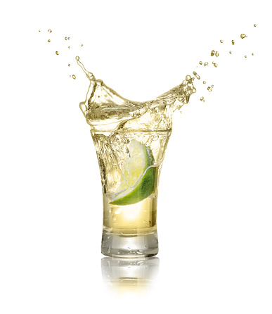 gold tequila shot with lime slice and splash isolated on white background. Lime is falling in the alcohol drink. Splash of tequila from the falling piece of lime