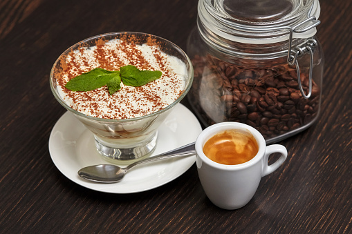 Tiramisu creme cake dessert in glass with mint leaves and coffee cup on black wooden background