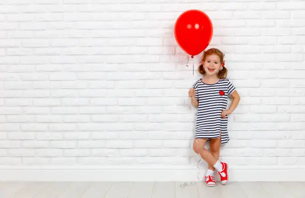 Photo of Happy funny child girl with  red ball near an brick wall