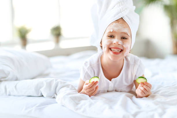 happy child girl in towel with mask on face - facial mask spa treatment cucumber human face imagens e fotografias de stock