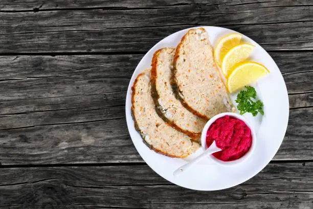 Jewish whitefish or minced-fish forcemeat stuffed inside the fish skin, cut in slices and served  with lemon slices and horseradish flavored with beetroot, authentic recipe, view from above