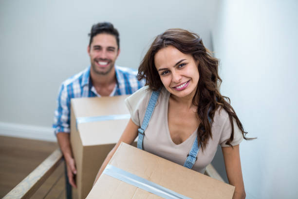 istock Portrait of smiling couple holding cardboard boxes while climbing steps 675583214