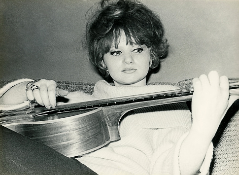 Vintage black and white photo from the sixties of a young woman playing guitar.