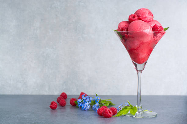 Raspberry ice cream sorbet in glass with raspberry, mint leaves  copy space on grey textured background