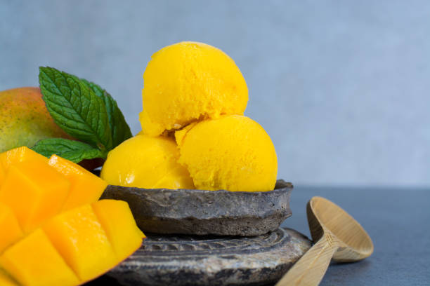 istock Mango ice cream sorbet with mint leaves and mango fruit in black stone bowl on grey textured backgund 675638140