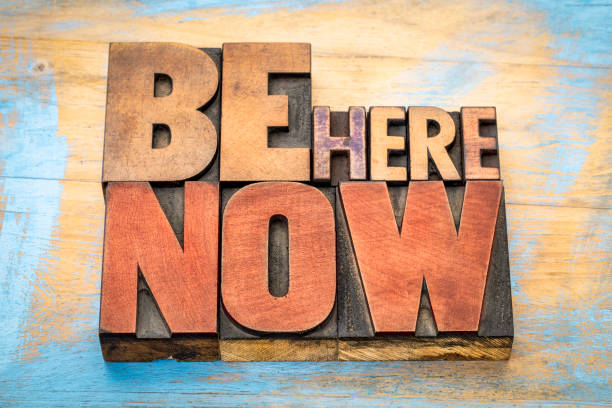 istock Be here now word abstract in wood type 675643518
