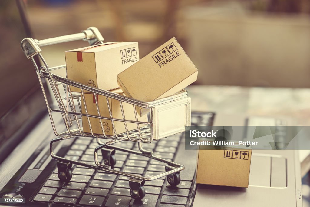 Paper boxes in a shopping cart. Paper boxes in a shopping cart on a laptop keyboard. Ideas about e-commerce, e-commerce or electronic commerce is a transaction of buying or selling goods or services online over the internet. Merchandise Stock Photo