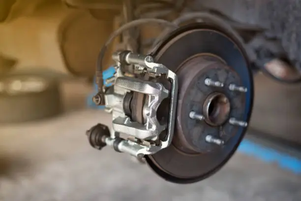 Photo of car wheel brake disc and shoes of lifted automobile at repair service station