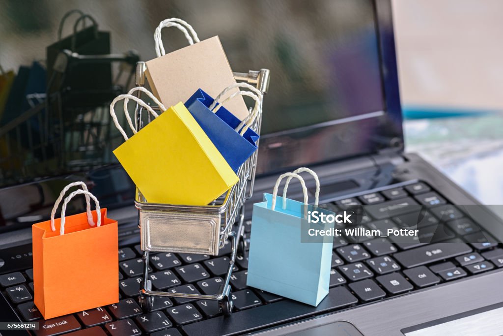 Five paper shopping bags and a shopping cart on a laptop keyboard. Five paper shopping bags and a shopping cart on a laptop keyboard. Concept about online shopping that customers can buy everything from home or office and the messenger will deliver to the doorstep. Online Shopping Stock Photo