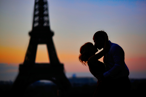Silhouettes of a romantic couple kissing in front of the Eiffel tower at sunrise in Paris, France