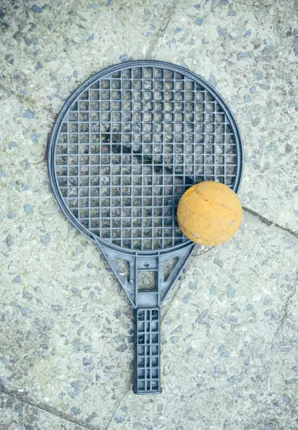 Round silver plastic toy bat and yellow tennis ball lying on mottled floor tiles viewed from above in a concept of sport and recreation